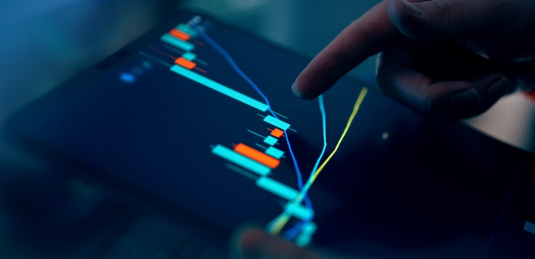 Close-up of a finger pointing at a digital trading chart with colorful candlestick patterns on a tablet screen.